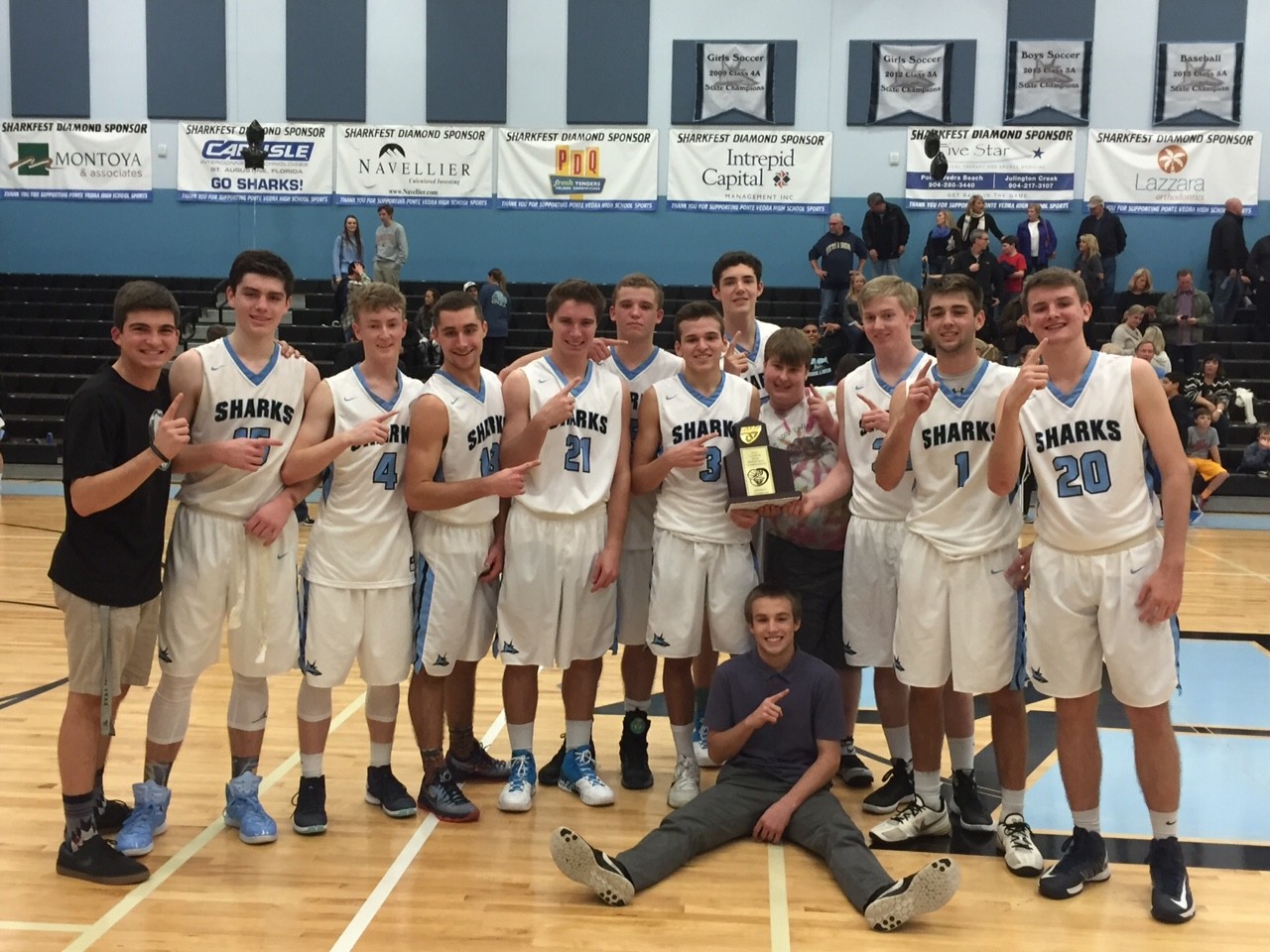 The Sharks varsity basketball team celebrates their third district championship in five years with their manager.