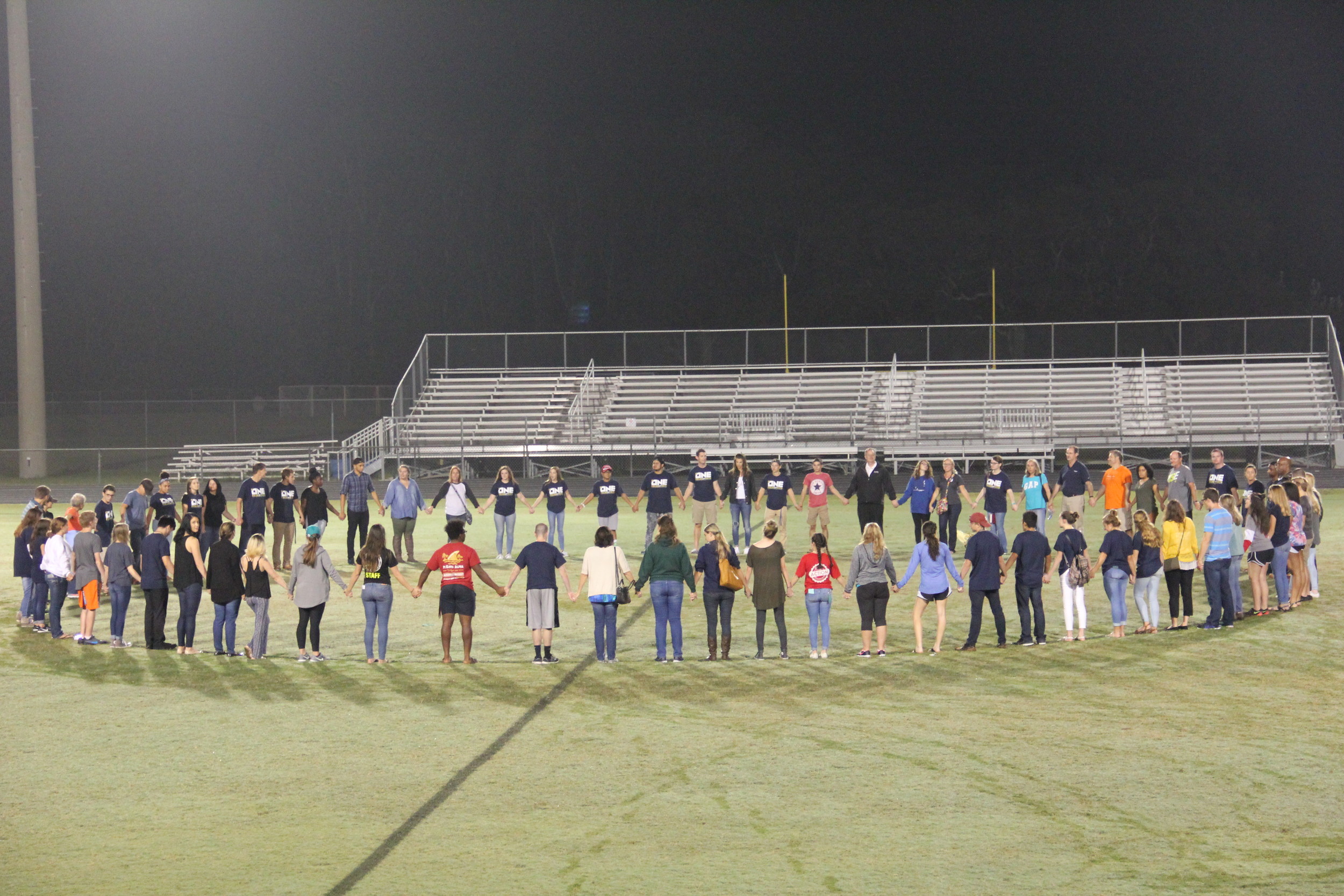 Fields of Faith participants gather in a circle center field to close the event in prayer.