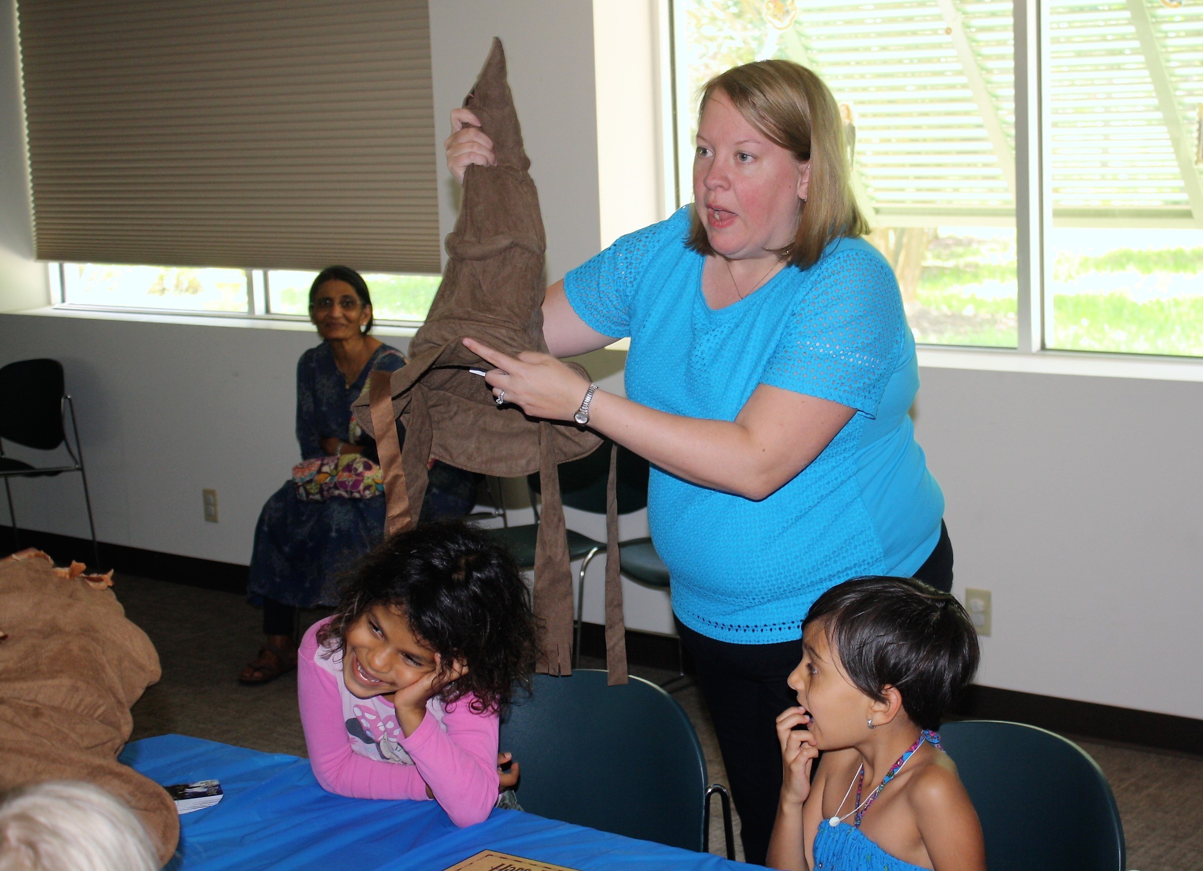 Youth Services Librarian Anne Crawford places the sorting hat on a child's head.