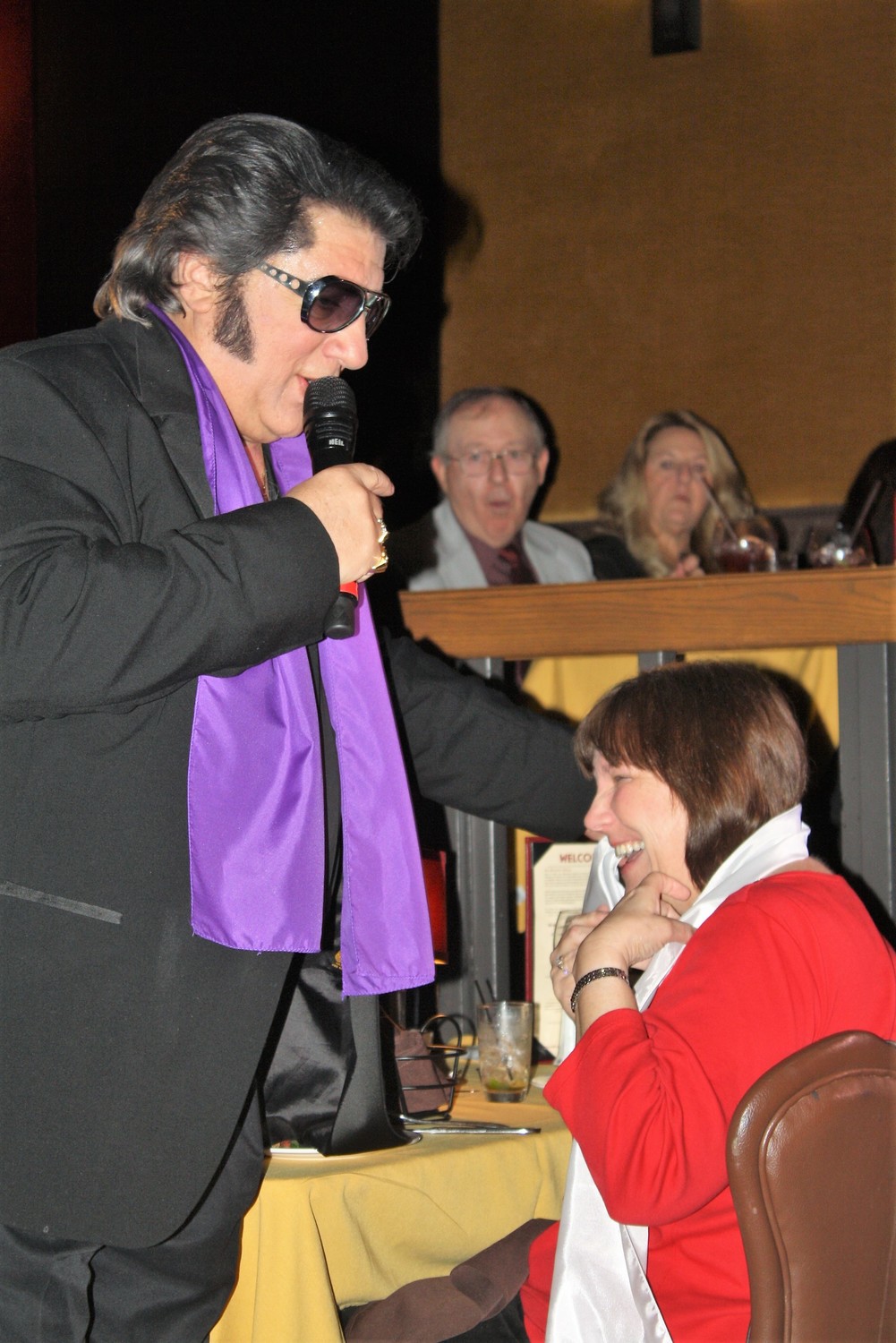 Elvis Presley (portrayed by Rick Marino) works the crowd, bestowing an audience member with a scarf.