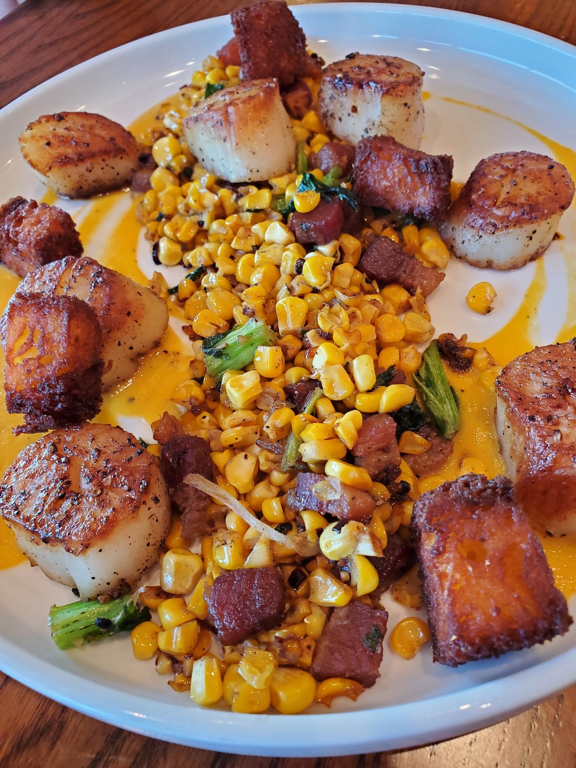 Chef Mike Cooney’s unique interpretation of scallops this season features corn: seared scallops with sweet corn puree, chewy roasted fresh corn, crispy cubed corn bread, mustard greens and bacon lardon.