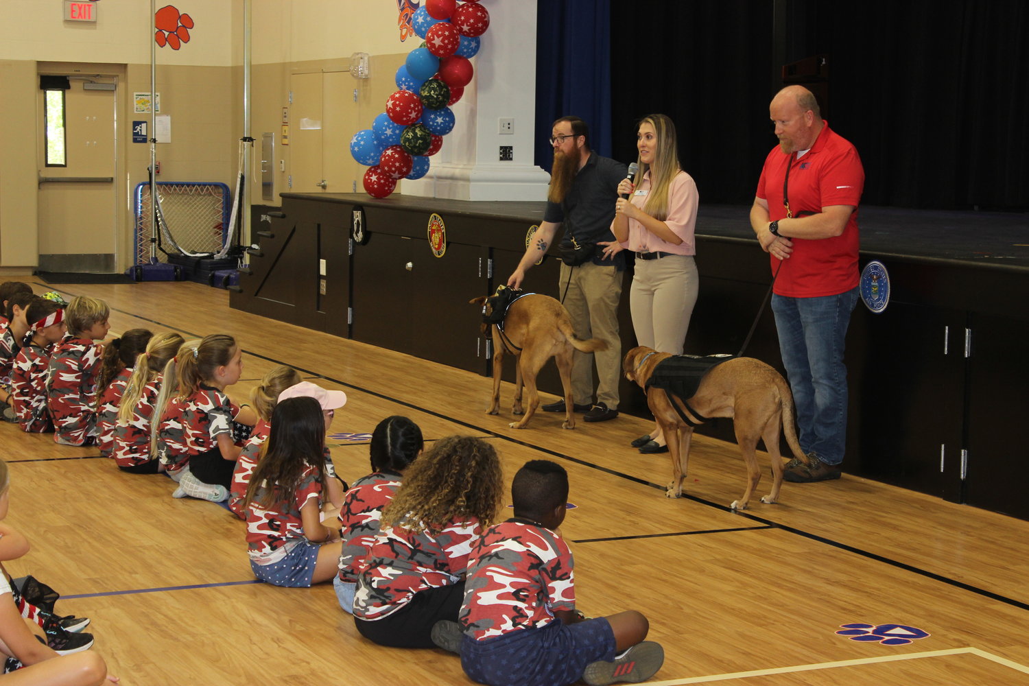 James Rutland with Dunkin, K-9s For Warriors senior development specialist Carly Braun and Greg Wells with Utah, from left, speak to students at The Bolles Lower School Ponte Vedra Beach Campus during field day on May 6.