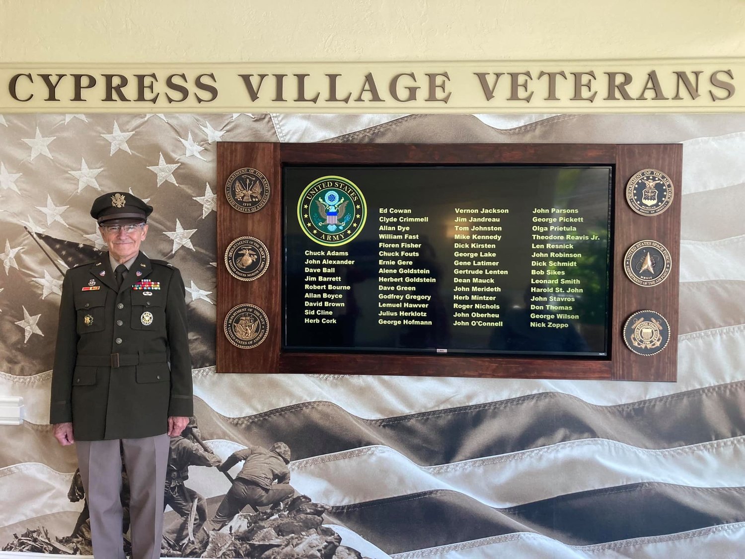 Veterans Committee chair Jim Jandreau stands next to the Veterans Recognition Wall at Cypress Village.